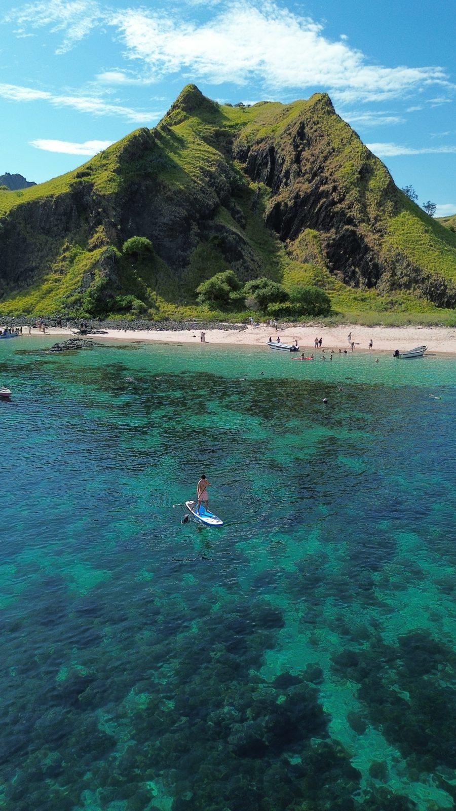 Kelor – paddleboarder off steep green hill island (Echtes Foto von einer Komodo-Explorer-Fahrt)